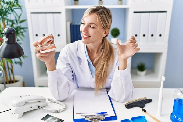 stock image Young blonde woman wearing dentist uniform holding brackets and invisible aligneer at clinic