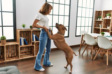 Beyaz bir kadın gülümseyerek evde köpekle dans ediyor.