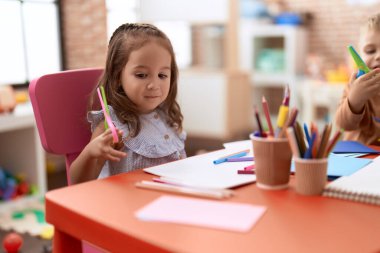 Adorable girl and boy sitting on table cutting paper at kindergarten