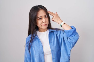 Young chinese woman standing over white background shooting and killing oneself pointing hand and fingers to head like gun, suicide gesture. 