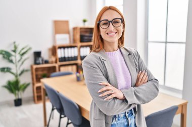 Beyaz kadın iş kadını gülümseyen, kendine güvenen, kollarını kavuşturup ofiste el kol kola duran.
