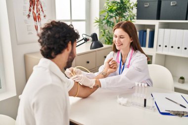 Doktor üniforması giyen kadın ve erkek klinikte kan tahlili yaptırıyor.