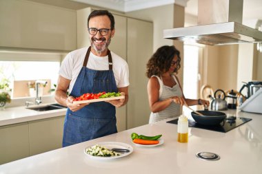 Orta yaşlı bir çift evde Akdeniz yemeği pişiriyor kameraya seksi bir ifadeyle bakıyor, neşeli ve mutlu bir yüzle.. 