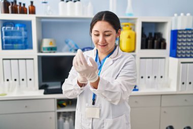 Young hispanic woman wearing scientist uniform and gloves at laboratory
