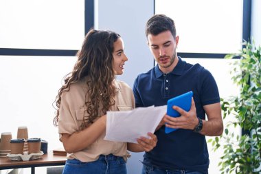 Young hispanic couple business workers using touchpad reading document at office