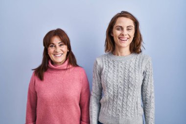 Mother and daughter standing over blue background with a happy and cool smile on face. lucky person. 