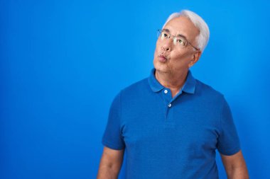 Mavi arka planda gri saçlı orta yaşlı bir adam dudaklarıyla balık suratı yapıyor, çılgınca ve komik bir jest. Komik ifade. 