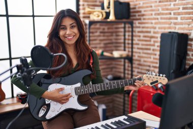 Young hispanic woman artist playing electrical guitar at music studio