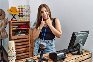 Perakende dükkanında açık mesajla pankart tutan genç esmer kadın ağzı açık gülümsüyor, parmakları işaret ediyor ve neşeli bir gülümseme sergiliyor. 