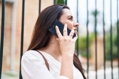 Genç, güzel, İspanyol bir kadın gülümsüyor ve caddede akıllı telefondan konuşuyor.