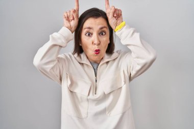 Orta yaşlı İspanyol bir kadın izole edilmiş arka planda duruyor ve boynuz gibi parmağıyla komik hareketler yapıyor. 