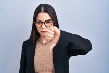 Mavi arka planda duran genç esmer kadın mutsuz ve kızgın görünüyor. Reddedilmiş ve olumsuz. kötü ifade. 