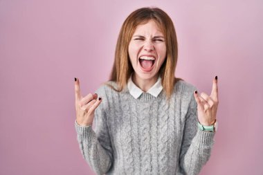 Pembe arka planda duran güzel bir kadın çılgın bir ifadeyle el kaldırarak rock sembolü yapıyor. Müzik yıldızı. ağır müzik konsepti. 