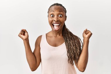 Örgülü siyah bir kadın, izole edilmiş arka planda durup kollarını kaldırarak ve gözlerini açarak başarının şokunu kutluyor. Kazanan konsept. 