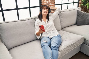 Genç, güzel İspanyol kadın evdeki kanepede müzik dinliyor.