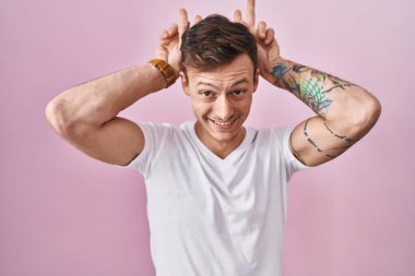 Caucasian man standing over pink background posing funny and crazy with fingers on head as bunny ears, smiling cheerful 