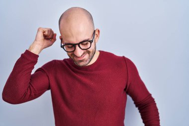 Beyaz arka planda duran sakallı genç adam gözlük takıyor mutlu ve neşeli dans ediyor, gülümsüyor rahat ve kendinden emin bir şekilde müzik dinliyor. 