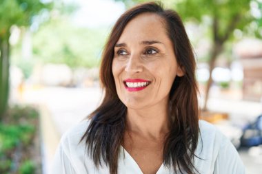 Genç, güzel, İspanyol bir kadın, gülümsüyor. Parkta kendine güveniyor.