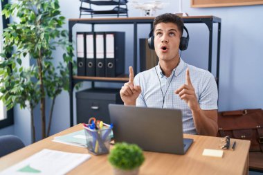 Ofiste çalışan genç İspanyol adam şaşırmış ve şaşırmış bir şekilde yukarı bakıyor ve parmaklarıyla işaret ediyor ve kollarını kaldırıyordu.. 