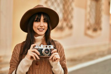 Kışlık şapkalı esmer kadın şehrin dışında klasik kamera kullanarak gülümsüyor.