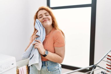 Genç kızıl saçlı kadın gülümsüyor. Kendine güveni tam. Çamaşırhanede yumuşak giysilerle yüzlere dokunuyor.