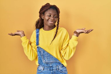 African woman standing over yellow background smiling showing both hands open palms, presenting and advertising comparison and balance 