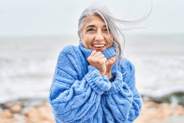 Orta yaşlı, kır saçlı, gülümseyen, kendine güvenen bir kadın.