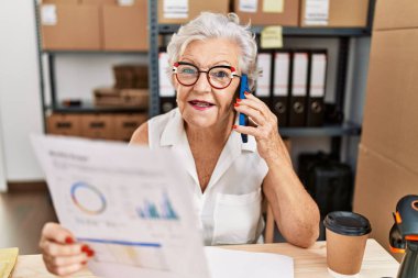 Ofisteki akıllı telefon okuma dokümanında konuşan kıdemli gri saçlı iş kadını.