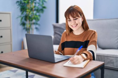 Evde dizüstü bilgisayar kullanan genç bir kadın.