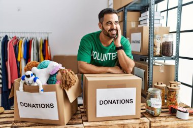 Hayır kurumunda bağış kutusuna yaslanmış gönüllü üniforması giyen İspanyol bir genç.