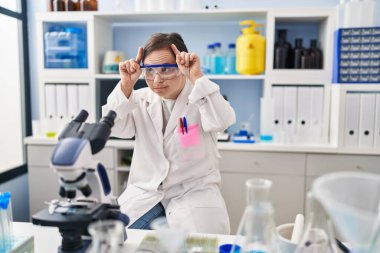 Down sendromlu İspanyol kız bilim adamı laboratuarında çalışıyor. Parmağını boynuzlarına geçirip komik jestler yapıyor. 