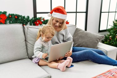 Mother and daughter using laptop sitting by christmas decor at home