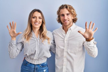 Young couple standing over blue background showing and pointing up with fingers number ten while smiling confident and happy. 
