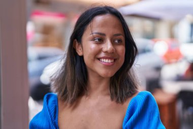 Genç İspanyol kadın gülümsüyor. Kendine güveni tam. Caddeye bakıyor.