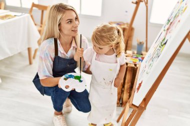 Anne ve kızı resim stüdyosunda kendine güvenen bir şekilde gülümsüyor.