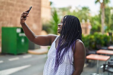 Afro-Amerikalı bir kadın, kahve dükkanının terasında kendine güvenerek gülümsüyor.