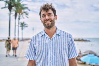 Genç İspanyol gülümseyen adam sahilde mutlu bir şekilde duruyor..