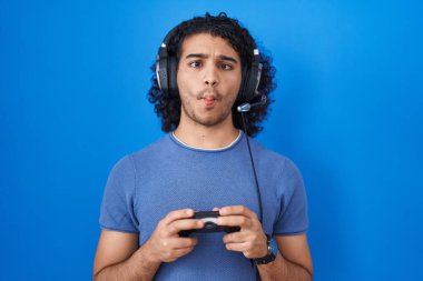 Kıvırcık saçlı İspanyol adam video oyunu oynuyordu. Kumandayı tutuyordu. Ağzı ve şaşı gözleriyle balık suratı yapıyordu.. 