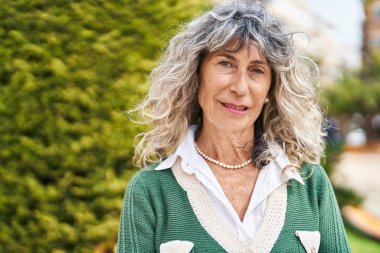 Parkta duran orta yaşlı, rahat yüzlü bir kadın.