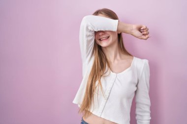 Pembe arka planda duran genç beyaz kadın kollarıyla gözlerini kapatıyor neşeli ve komik gülümsüyor. kör kavram. 