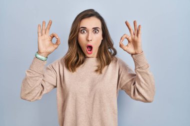 İzole edilmiş arka planda duran genç kadın şaşırmış ve şok olmuş görünüyor. Tamam sembolünü parmaklarıyla yapıyor. çılgın ifade 