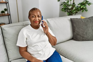 Kıdemli Afro-Amerikan kadın gülümsüyor evde akıllı telefondan konuşuyor.