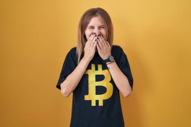 Bitcoin tişört giyen sarışın beyaz kadın gülüyor ve utanıyor kıkırdıyor ağızlarını ellerle, dedikodularla ve skandallarla örtüyor. 