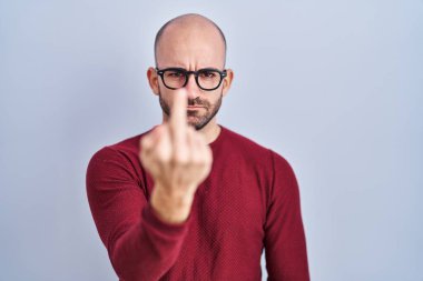 Young bald man with beard standing over white background wearing glasses showing middle finger, impolite and rude fuck off expression 