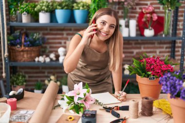 Çiçekçide, çiçekçide, güzel İspanyol bir çiçekçi akıllı telefondan not defterine yazı yazıyor.