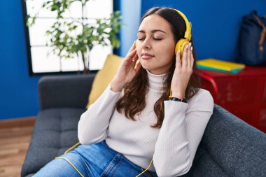 Genç, güzel, İspanyol bir kadın evdeki kanepede oturmuş müzik dinliyor.