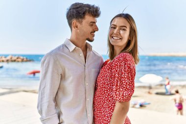 Genç İspanyol çift tatilde gülümsüyor ve sahilde birbirlerine sarılıyorlar.