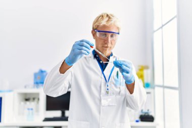 Laboratuvarda pipet kullanan, bilim adamı üniforması giyen beyaz bir genç.