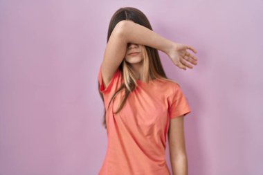 Pembe arka planda duran genç kız kollarıyla gözlerini kapatıyor, ciddi ve üzgün görünüyor. Görme, saklama ve reddetme konsepti 