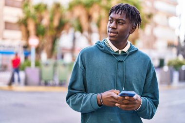 Sokakta akıllı telefon kullanan, kendinden emin gülümseyen Afrikalı Amerikalı bir adam.